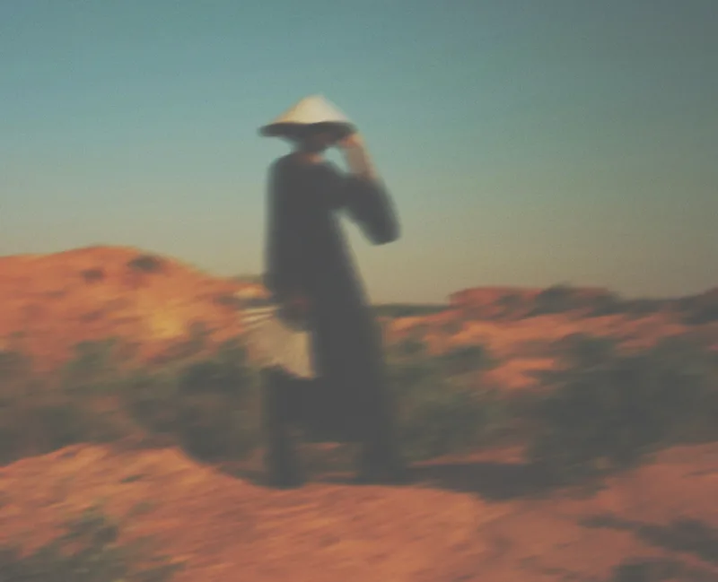 Blurred figure in a conical hat walking through dunes